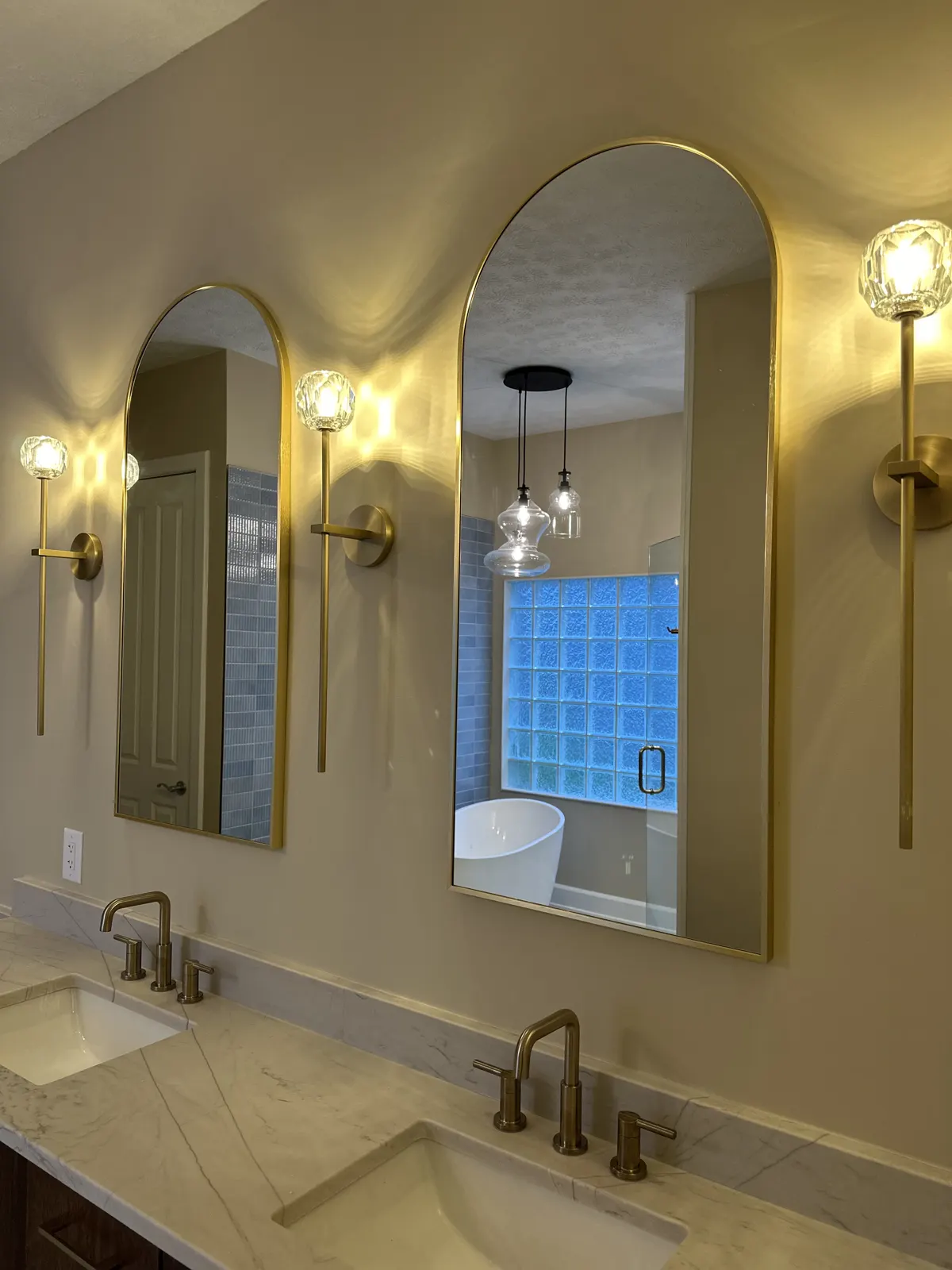 Arched mirrors and brass sconces over a quartz vanity