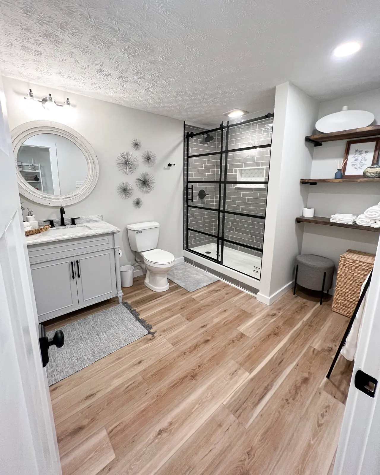 Hall bathroom with a black steel-frame shower, round mirror and open shelves