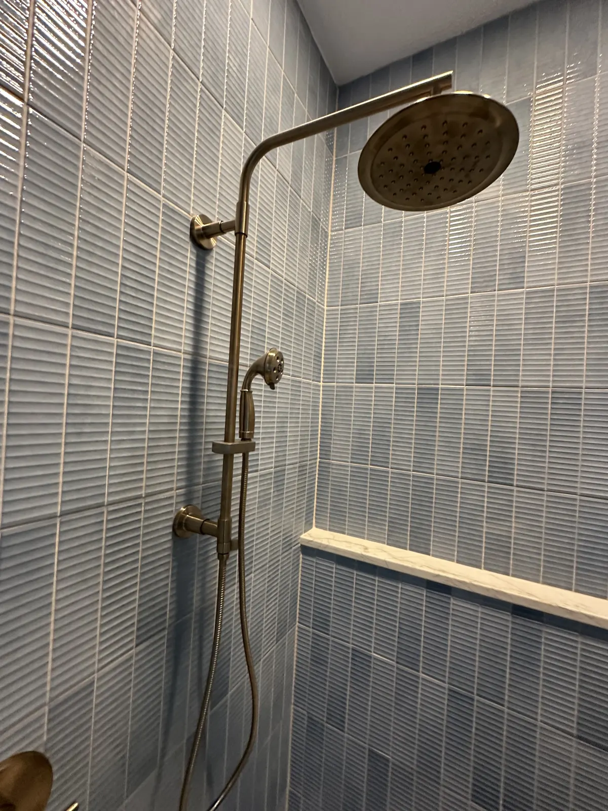 Brushed brass rain shower head and hand shower on blue vertical tile