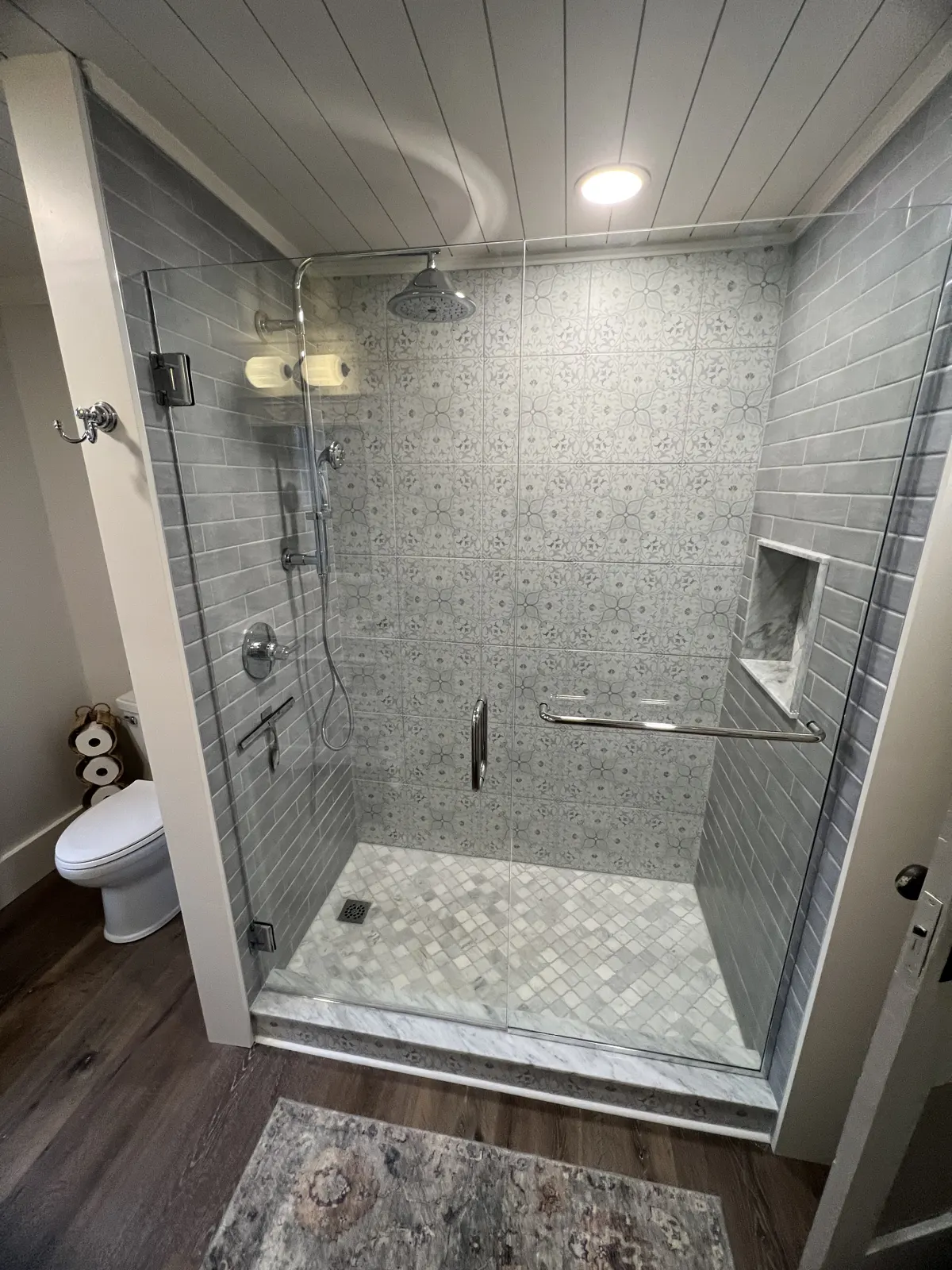 Walk-in shower with patterned gray tile and frameless glass under a shiplap ceiling
