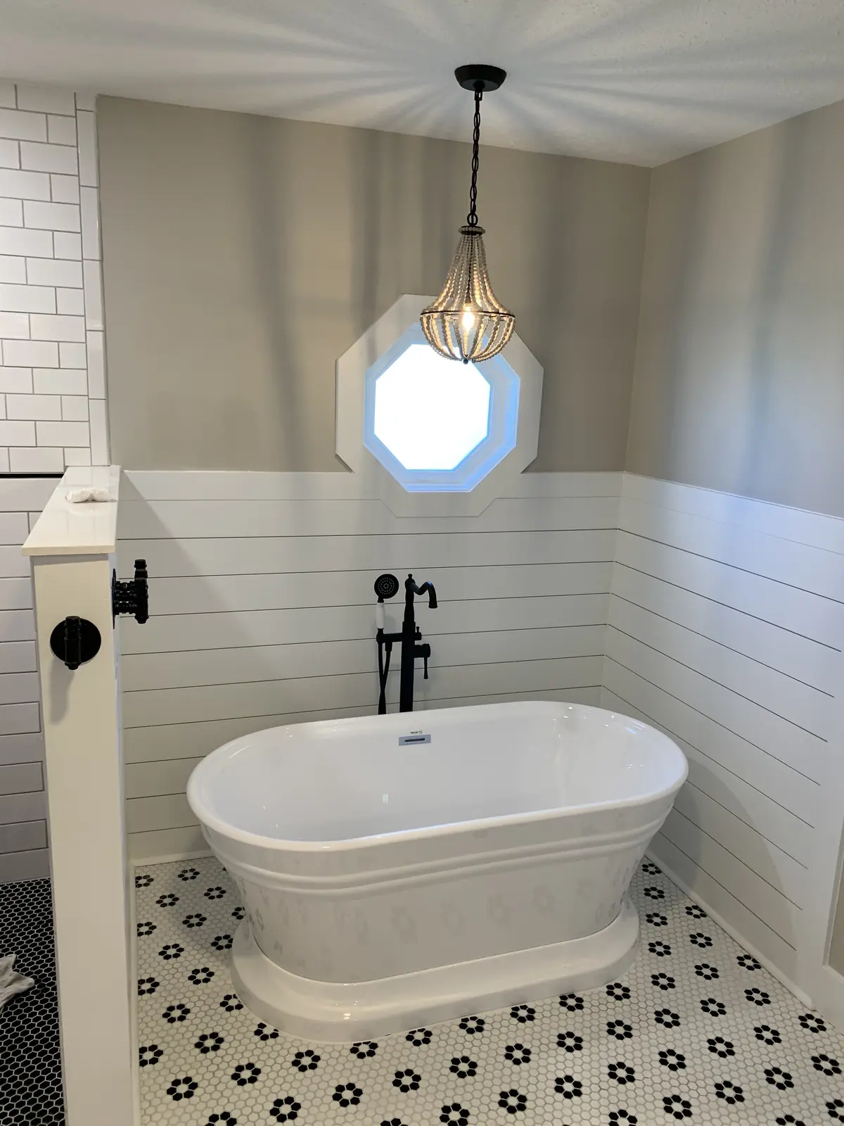 Freestanding tub under an octagon window with shiplap walls and a pendant light