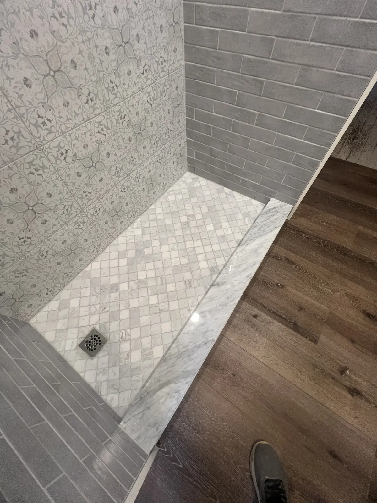 Marble mosaic shower floor meeting a wood-look floor
