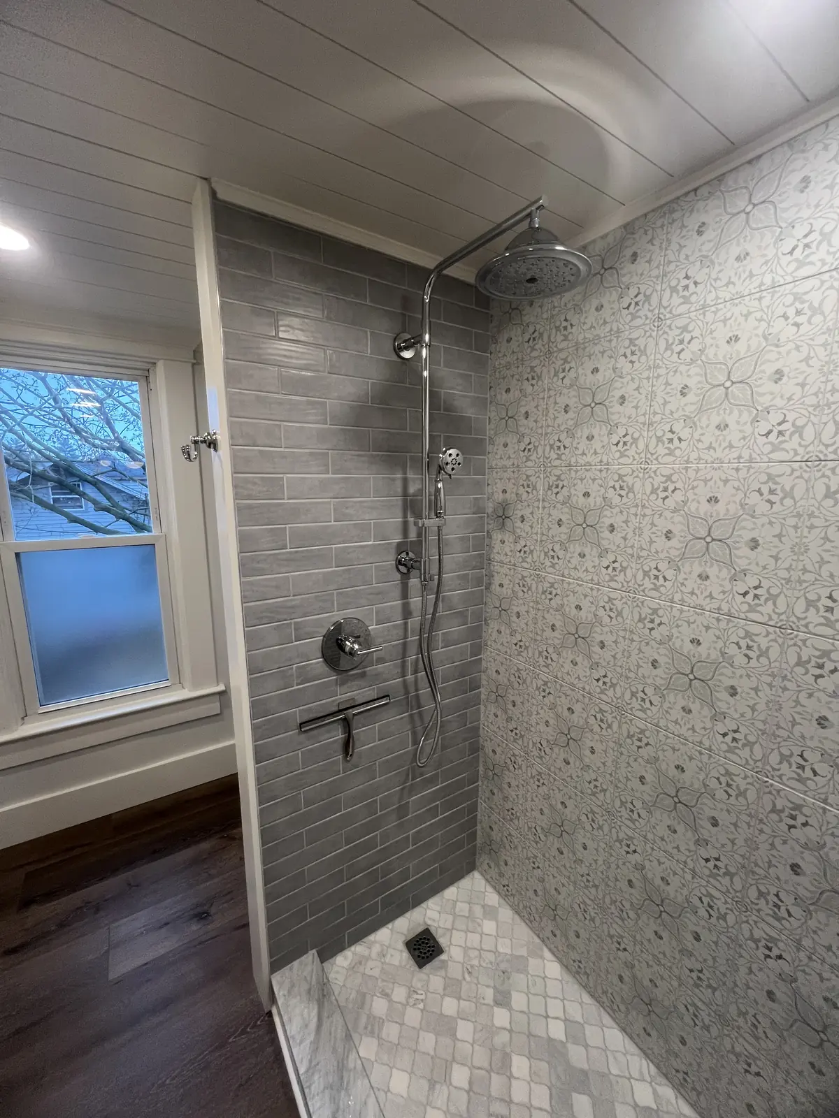 Patterned tile shower next to a window with a shiplap ceiling above