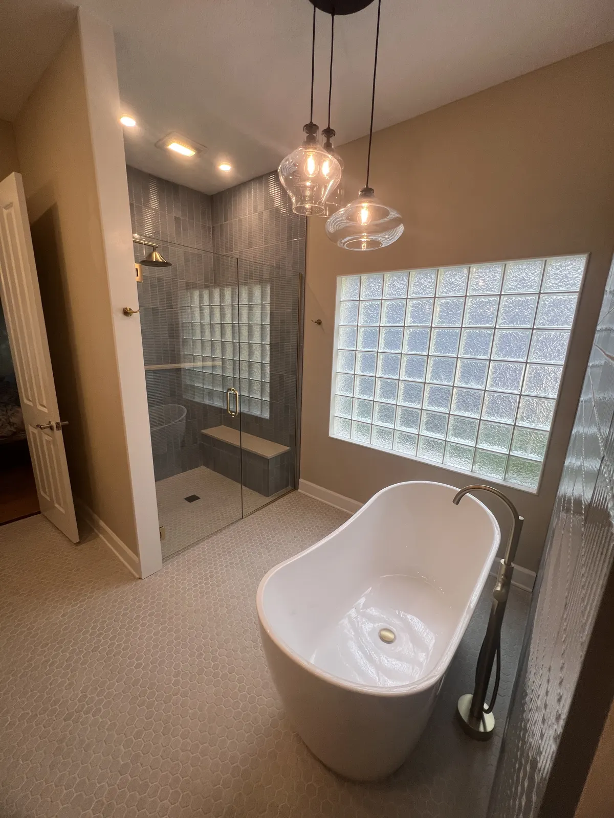Remodeled primary bathroom with tub under a glass block window and walk-in shower