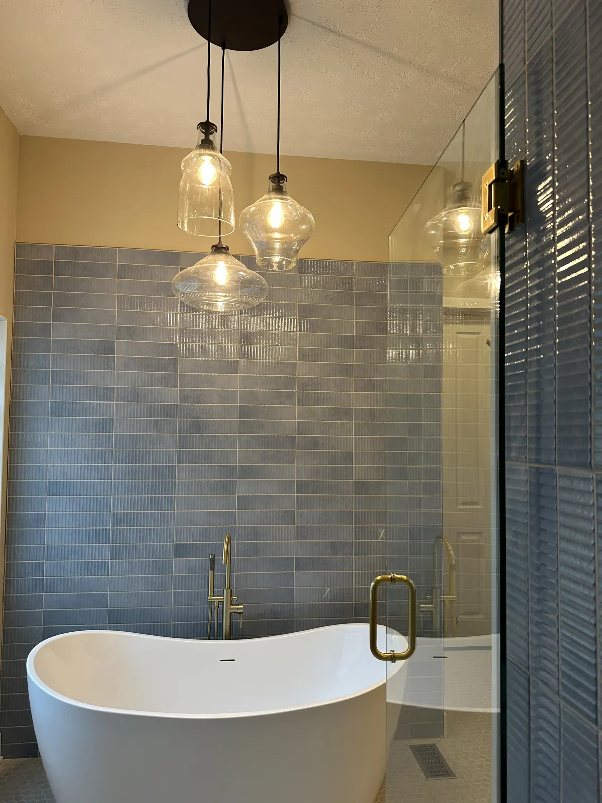 Soaking tub beneath three glass pendant lights and blue vertical tile