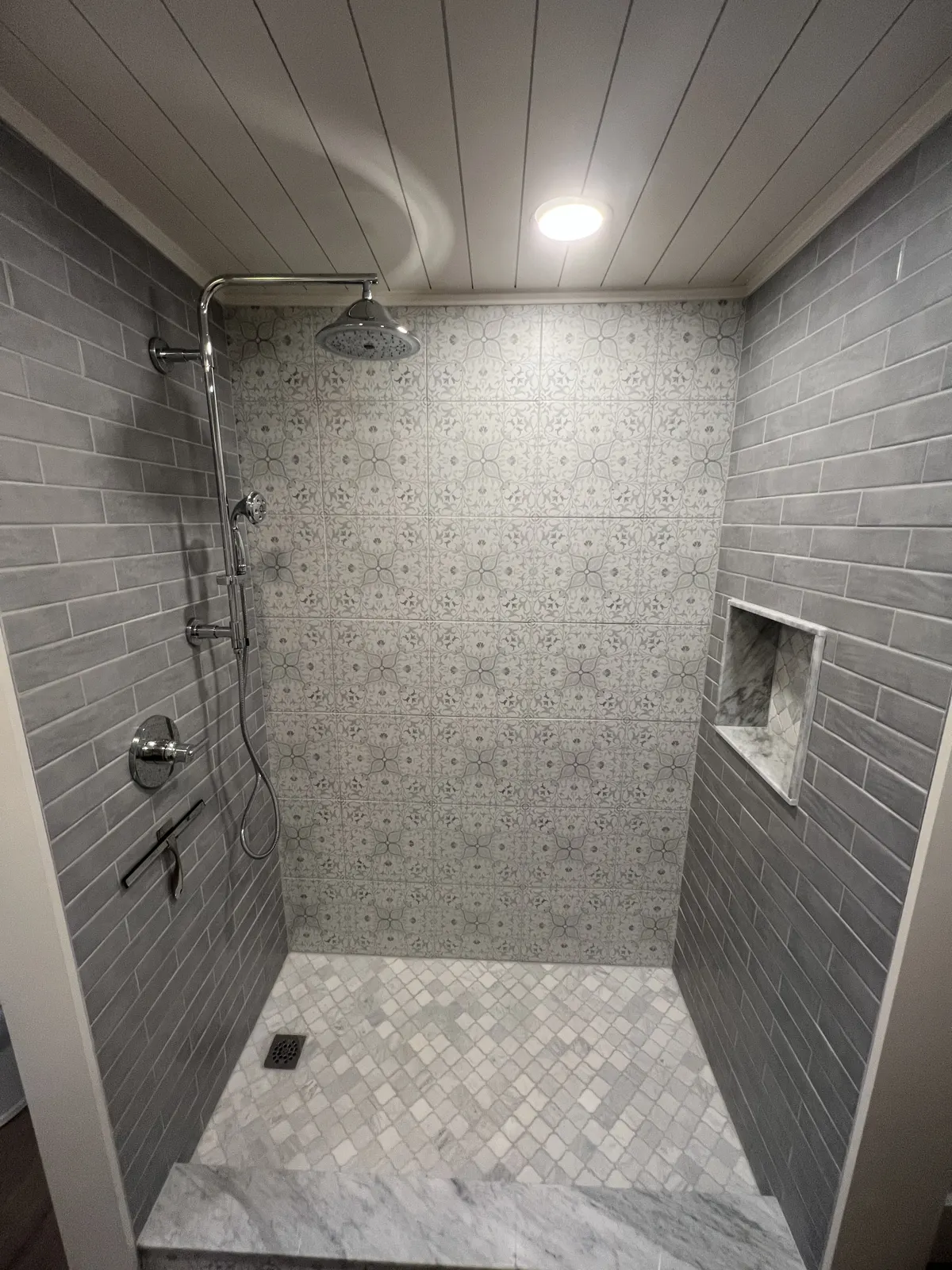 Walk-in shower with gray vertical tile and a recessed niche