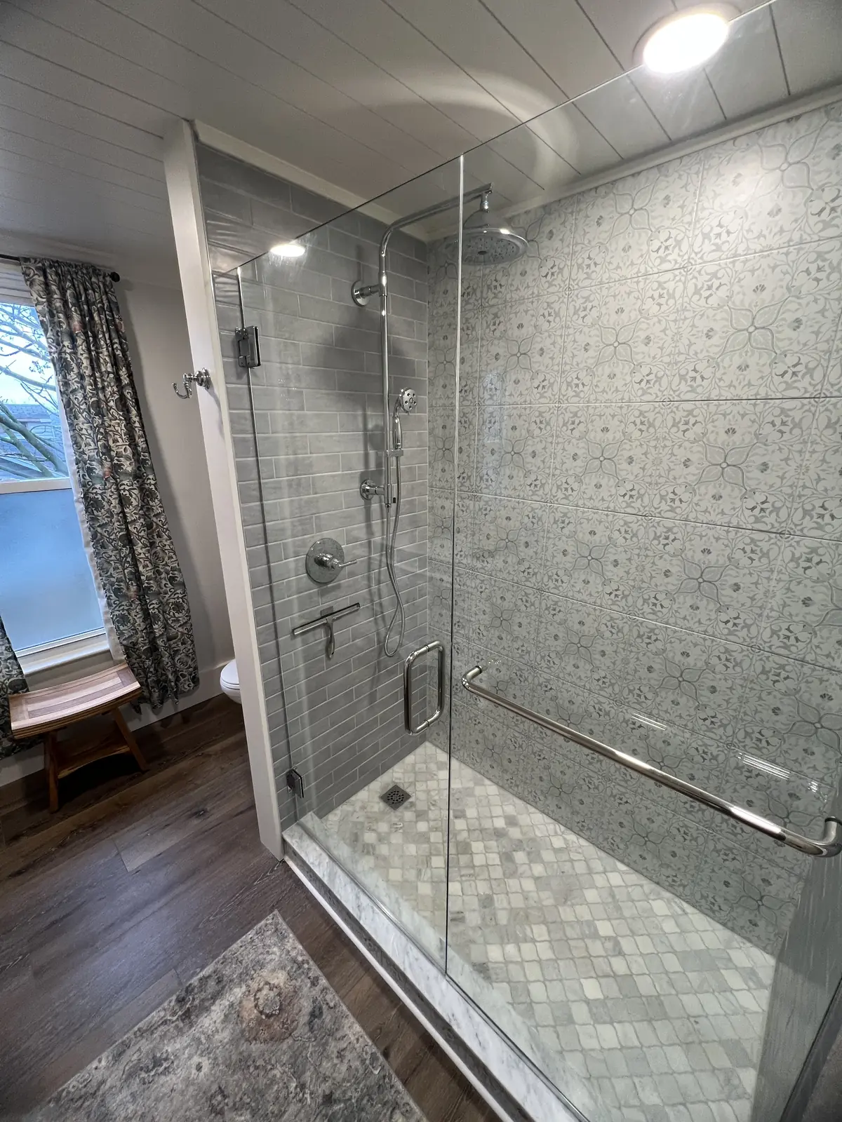 Walk-in shower with patterned gray tile, frameless glass and a window