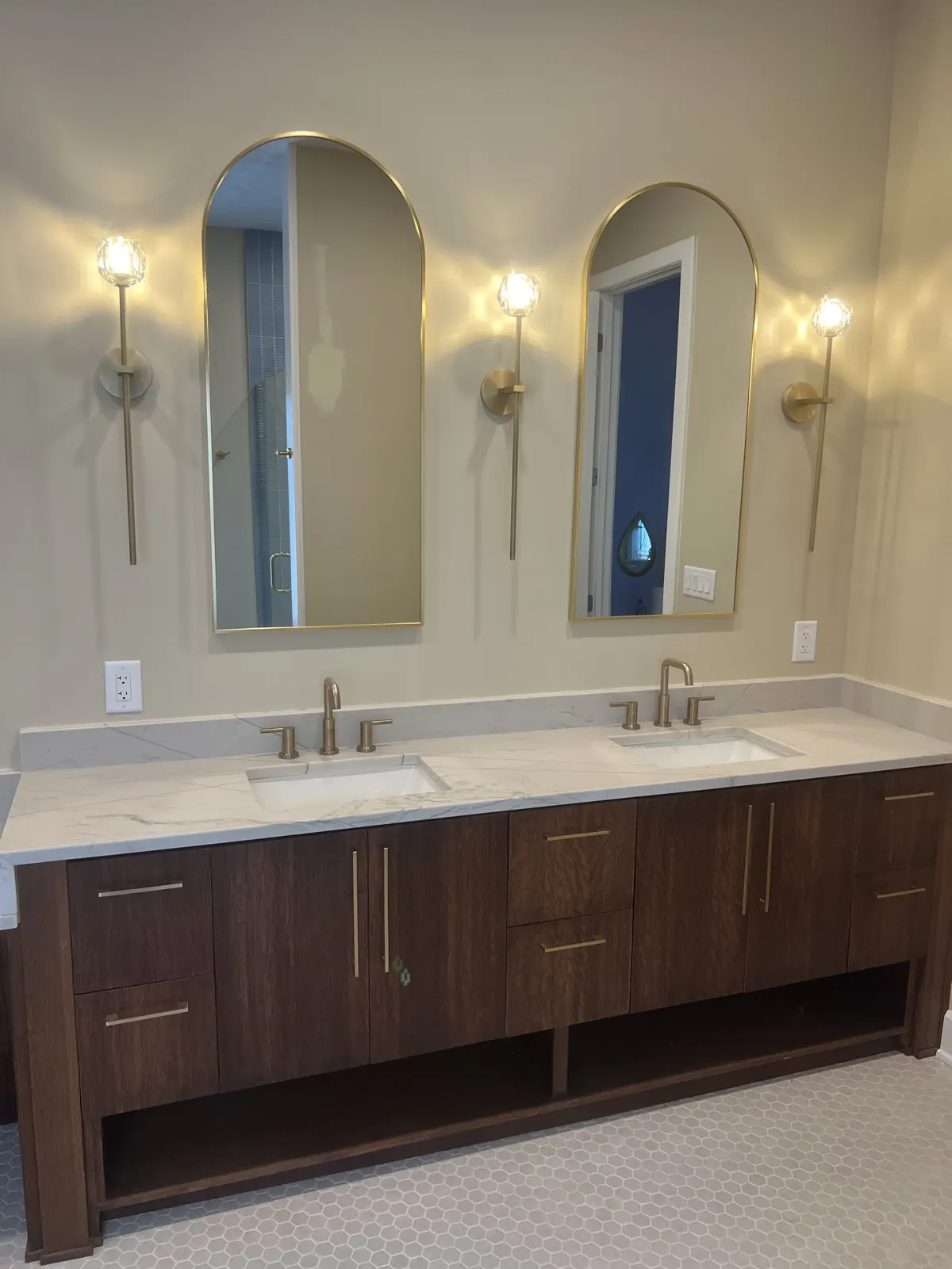 Walnut double vanity with arched mirrors and brass sconces